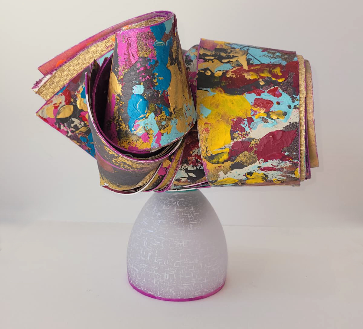 Vividly painted sculptural coil in magenta, gold, and turquoise on a white pedestal